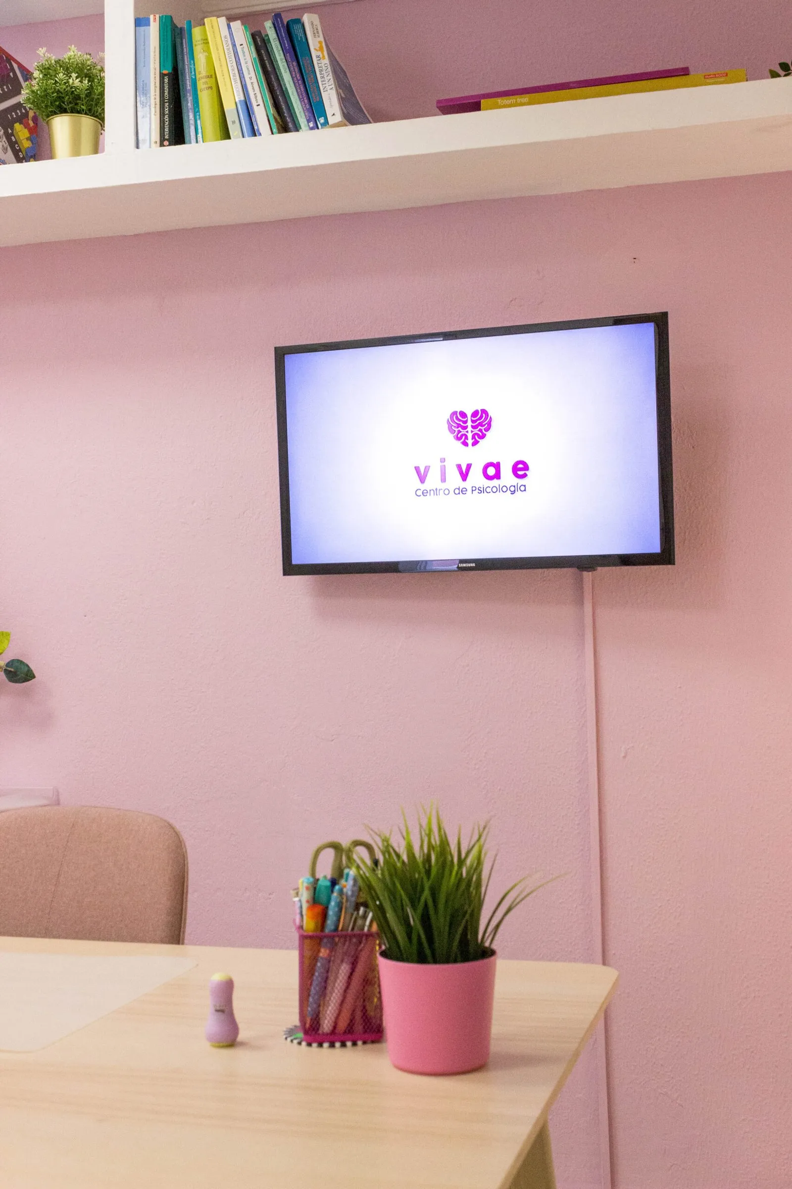 Pantalla en una pared rosa con el logo de Vivae Psicólogos