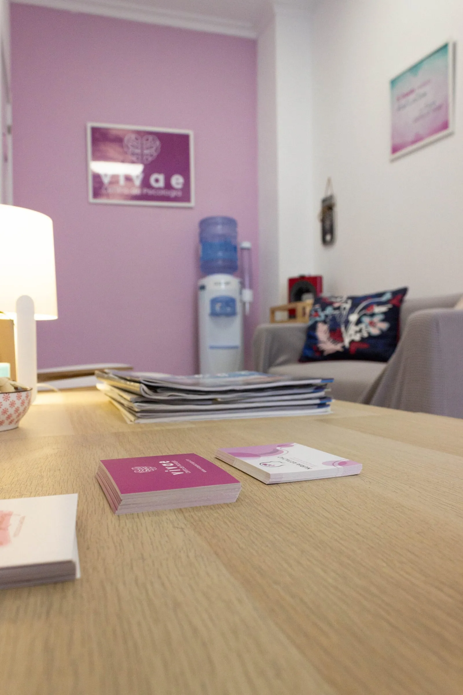 Sala de espera con revistas sobre una mesa, dispensador de agua y sofá con cojines