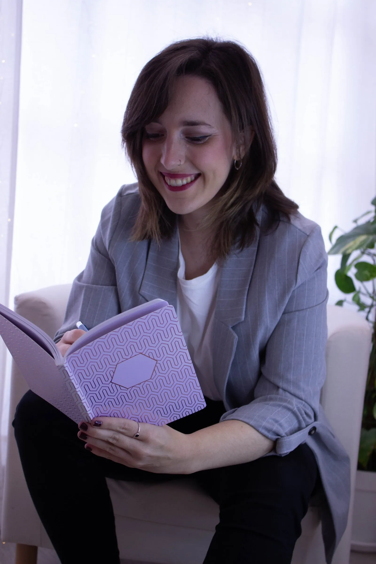 Sonia Ramírez sonriendo, sentada en un sillón y escribiendo en un cuaderno