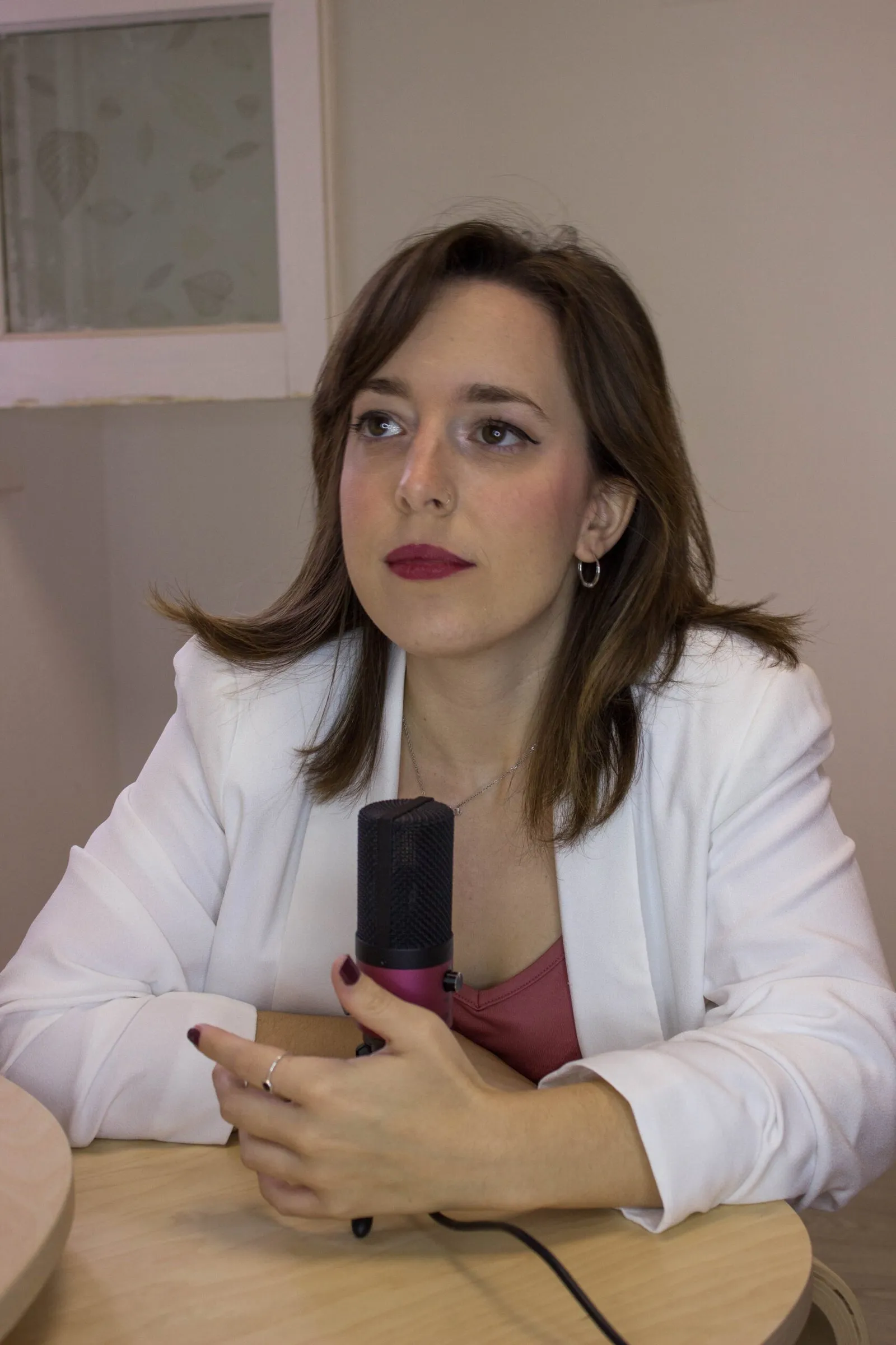 Sonia Ramírez con americana blanca, sentada a la mesa y hablando ante un micrófono